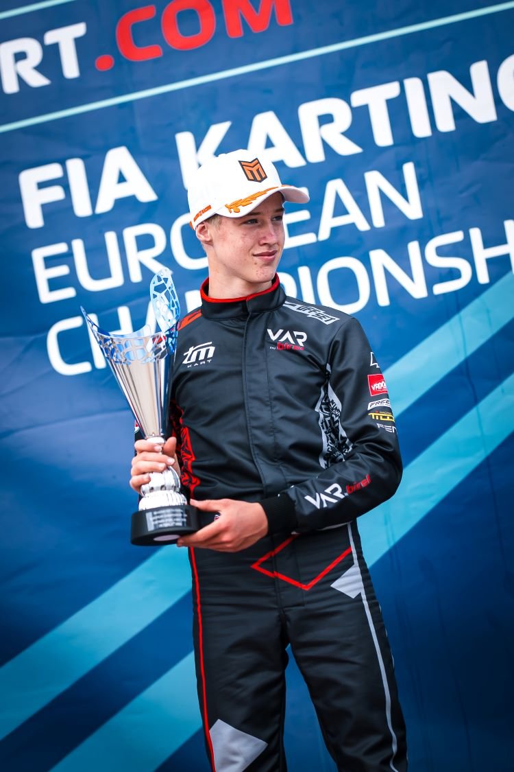 Noah Wolfe in FIA Karting race suit holding a winner's trophy